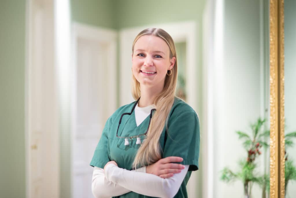 Portrait der lächelnden Dr. Lina Heurich in Arbeitskleidung vor verschwommenem Hintergrund im Praxisflur